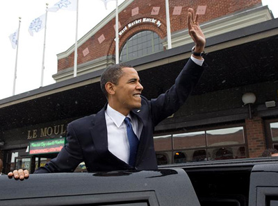 a smiling and happy president waving to the crowd in a car