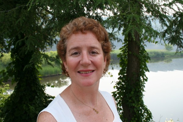 a woman smiling in front of some trees and water