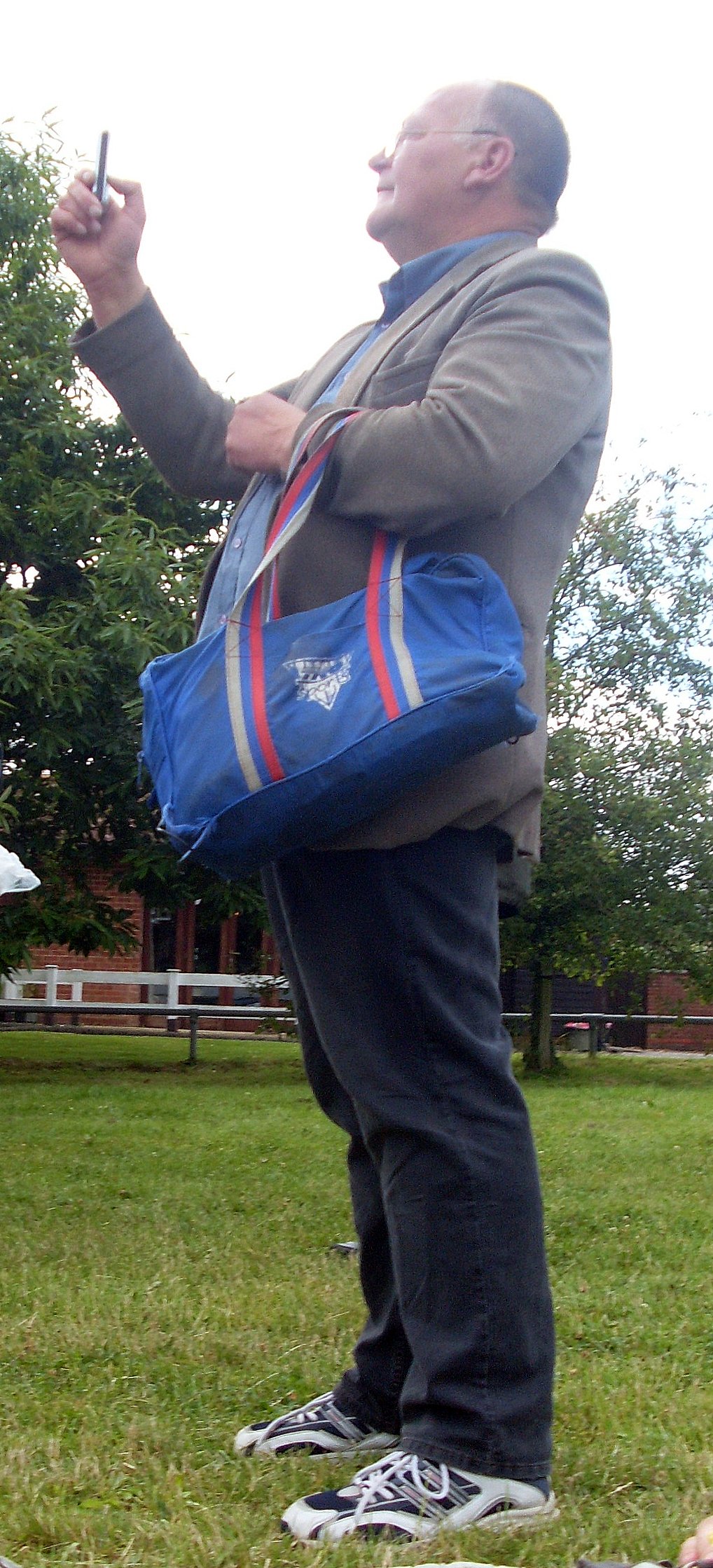 man standing in park smoking and holding blue bag