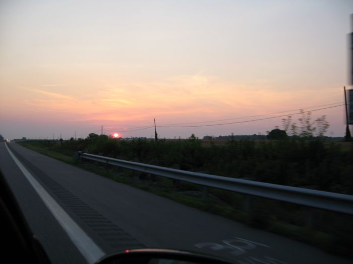the sun rising over the horizon of the street from a moving car