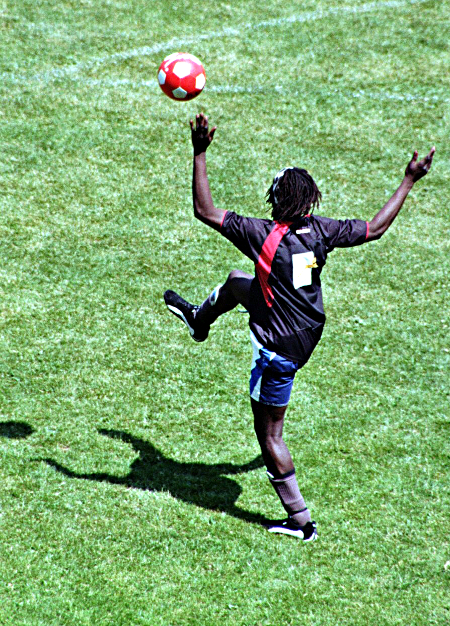 man in the field reaching out to catch a red soccer ball