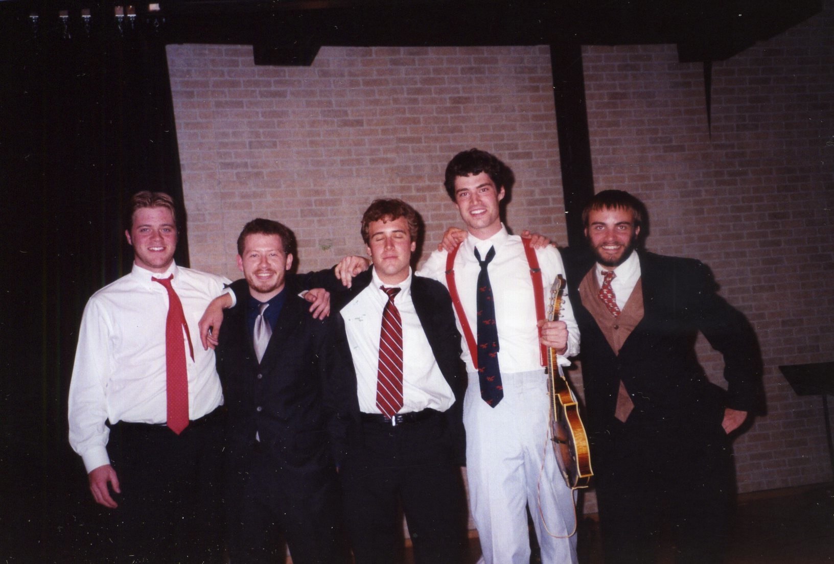 six men in dress suits standing in front of a wall