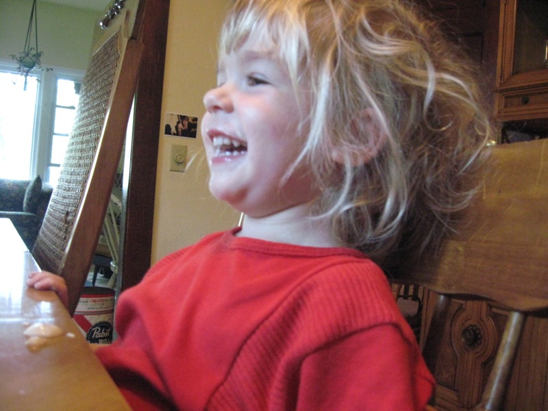 young blond girl with her fingers out sitting in chair smiling at camera