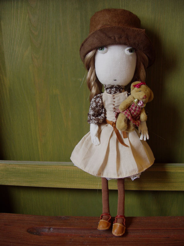 a doll with long blonde hair and brown shoes holds a teddy bear