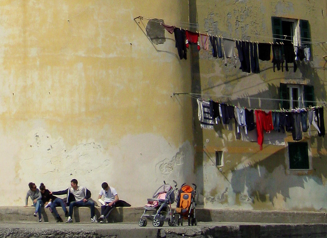 men sit by a dirty wall with clothes hanging