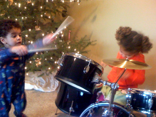 two children playing drum in front of the christmas tree