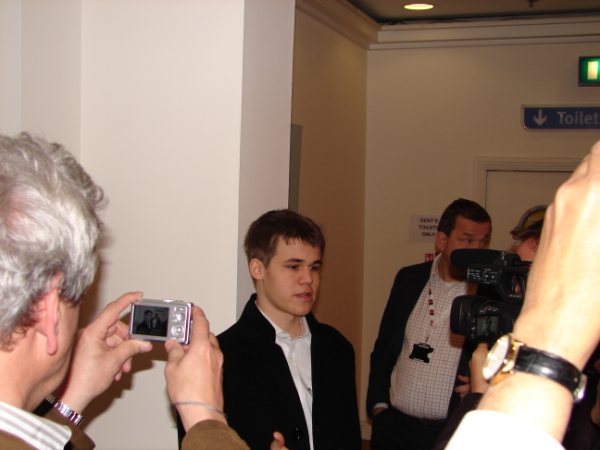 young man in suit and white shirt talking to a press camera while another person pographs him