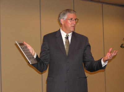a man in a suit and tie talking with an audience holding up a cell phone