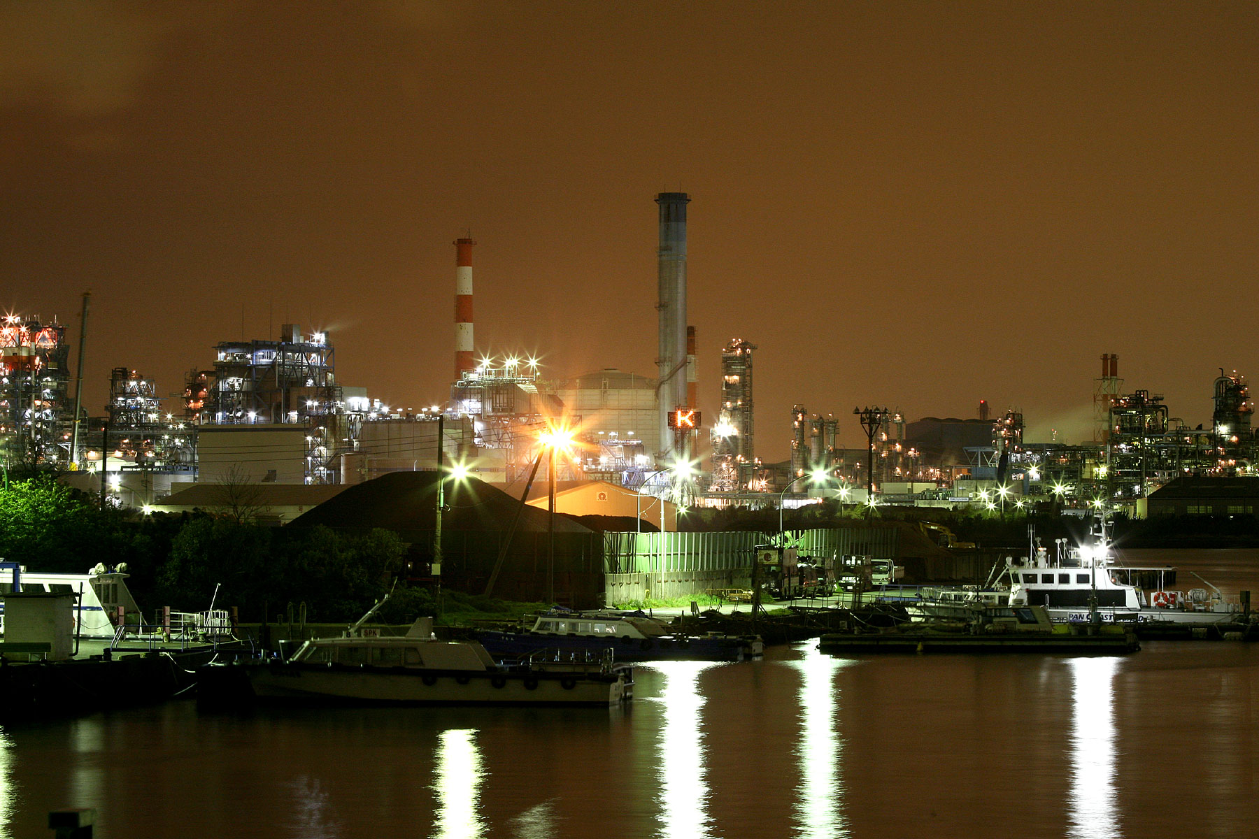 industrial area lit up at night with a boat and other boats in the water