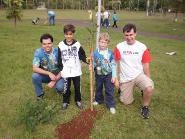 the family stands with one child and another boy next to a small tree