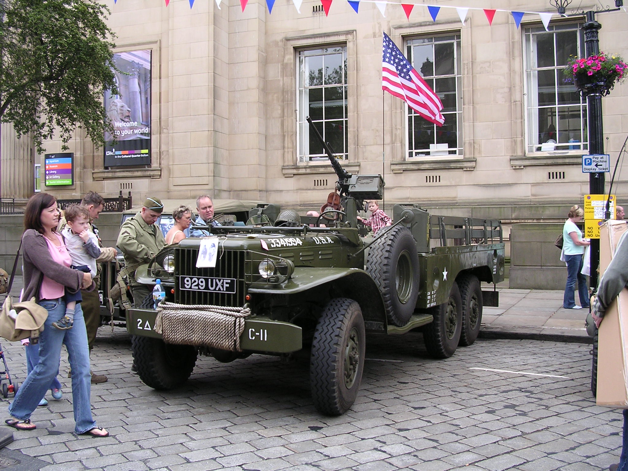 people stand around a green vehicle that is parked on a city street