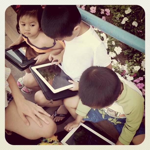 three children are sitting on a bench looking at ipads