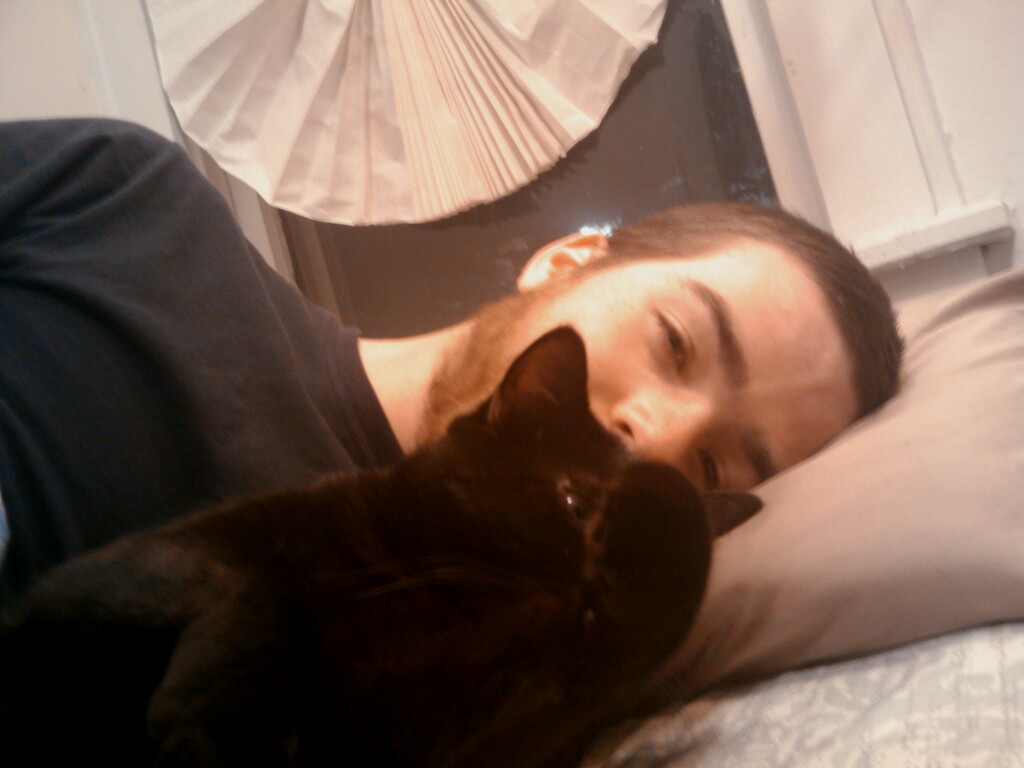 a person laying in bed with a black cat on his chest