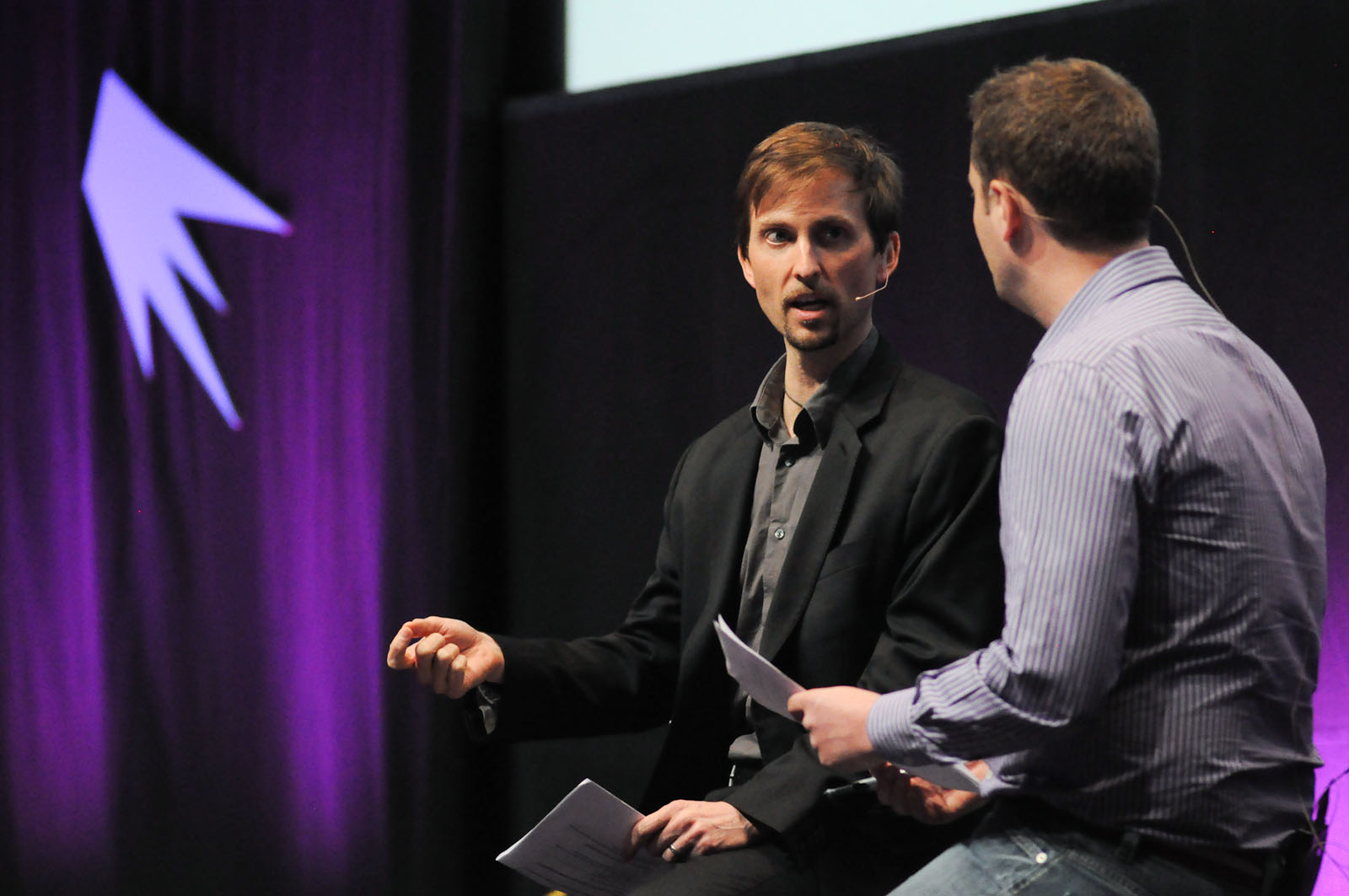 a man is talking to two other men on stage