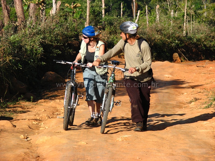 a couple of people standing with bikes on a dirt road