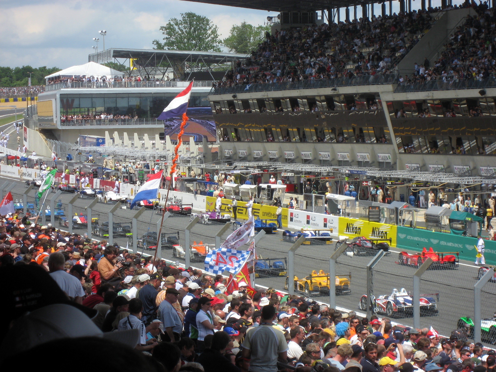 people sitting in front of a full stadium watching cars go by