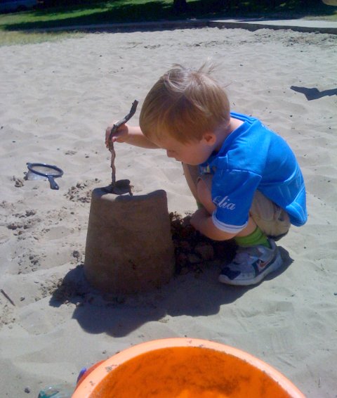 a small boy digging into a sandcastle on a beach