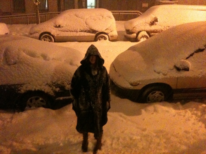 a woman in a hoodie standing in a parking lot near parked cars