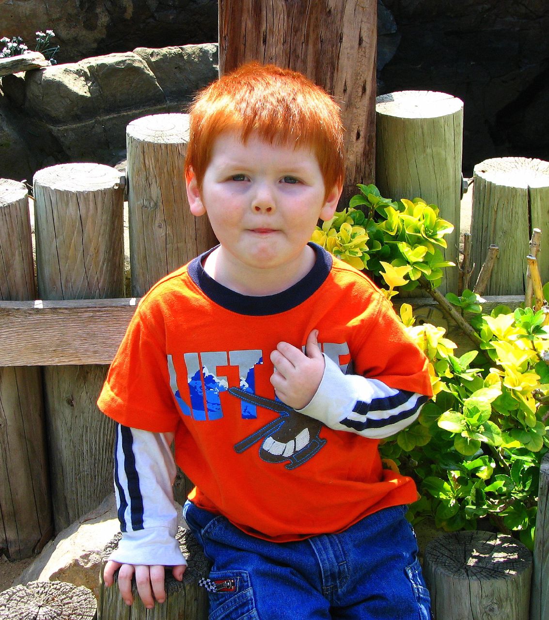 a small boy wearing an orange shirt next to a fence