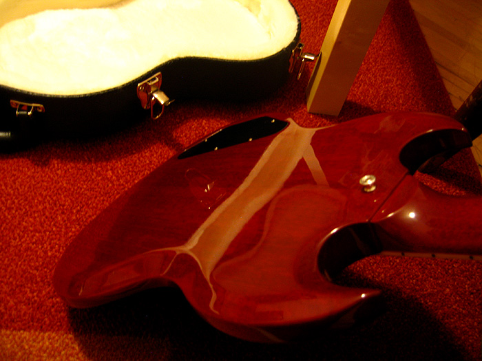 a cello case laying across a red carpet next to the guitar