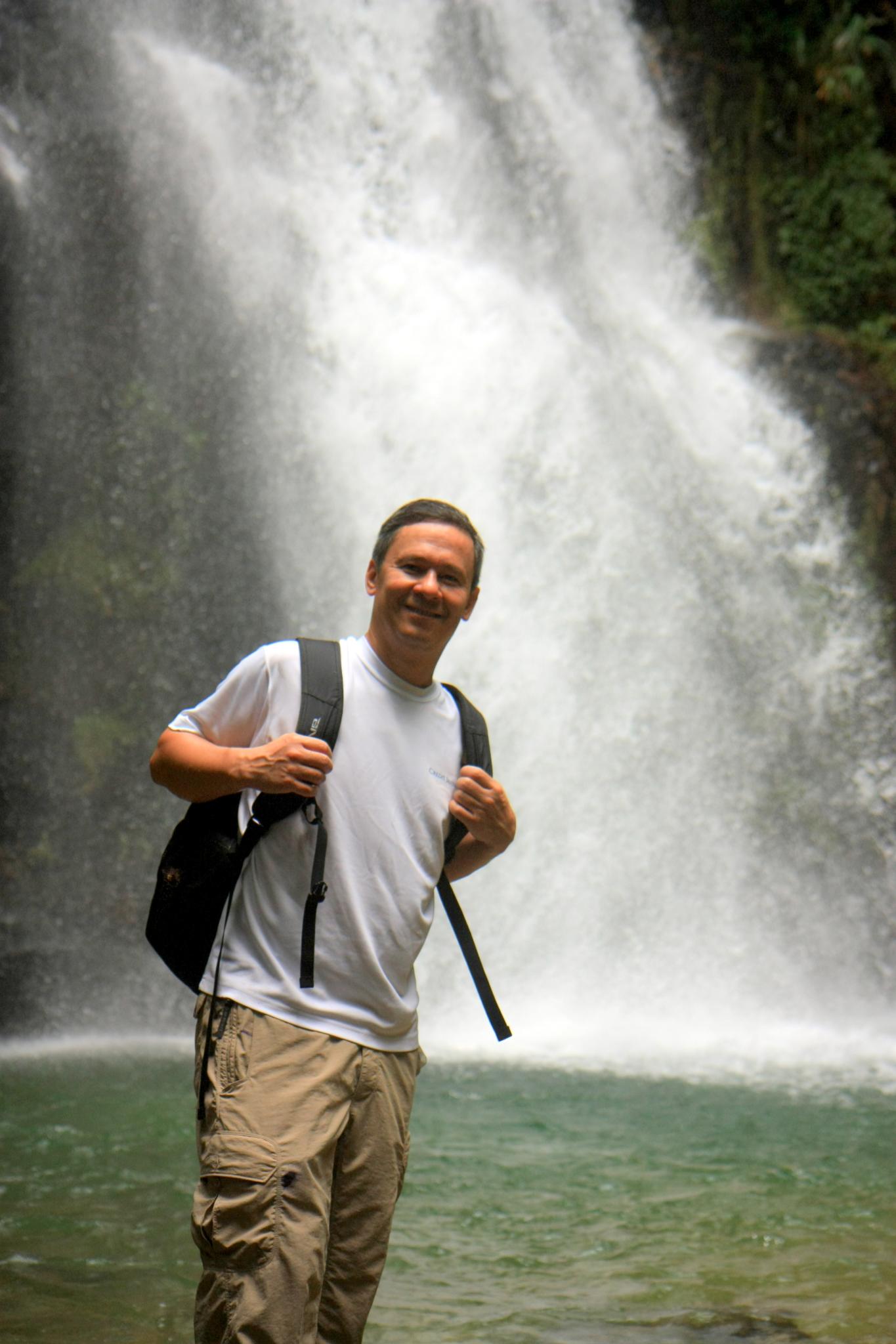 man with backpack standing in front of large waterfall