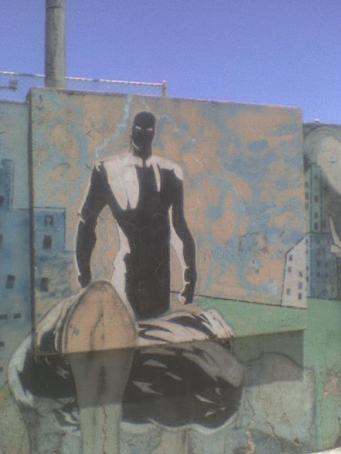 mural of a man sitting on a bench in front of a factory building