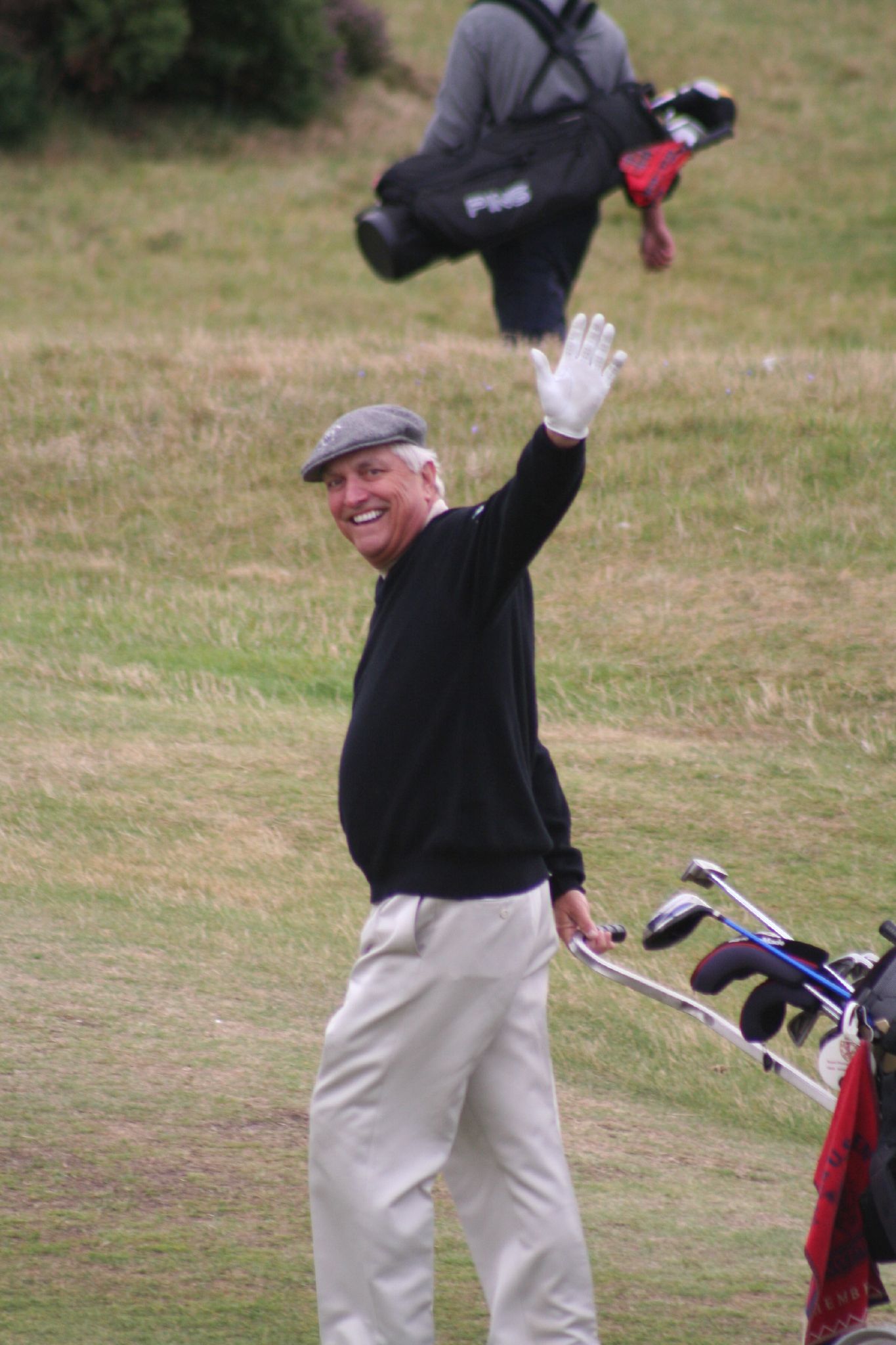 an old man waving in front of another man with his golf bag