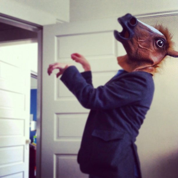 woman in jacket wearing a horse mask standing in front of doorway