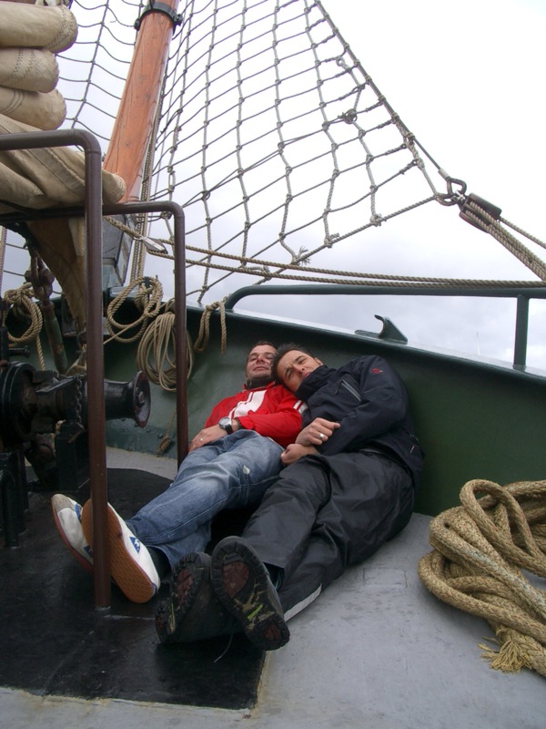 two men sitting on top of a boat on a pier