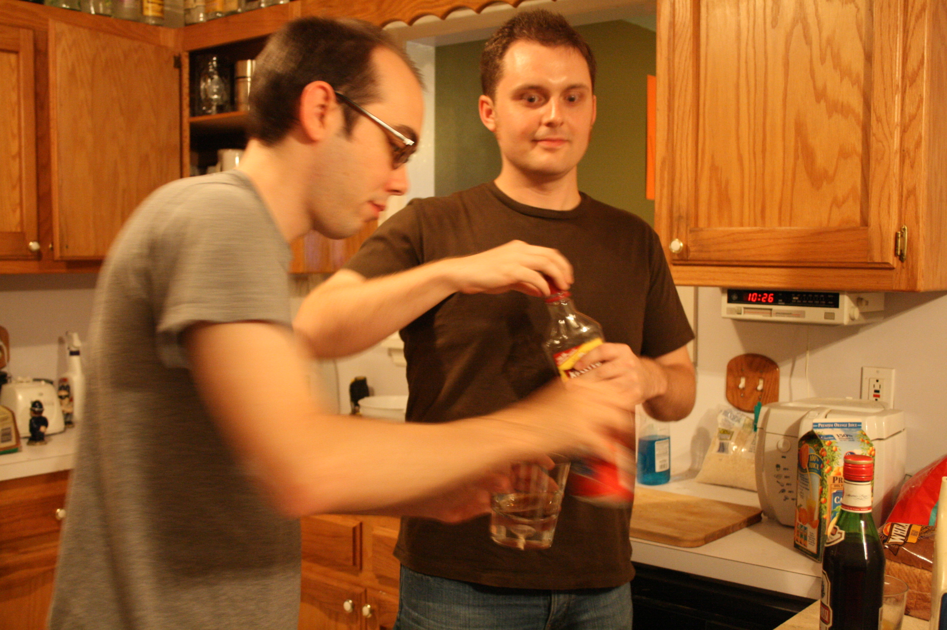 two men stand in a kitchen and drink a drink