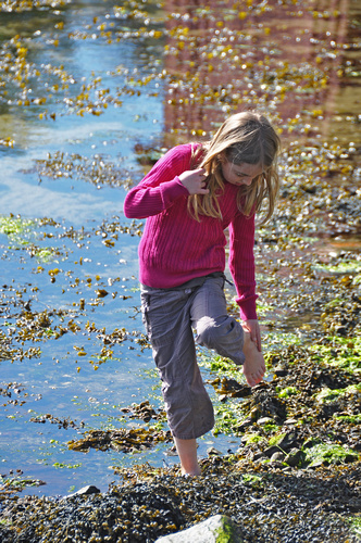  in pink shirt stepping on rocks next to river