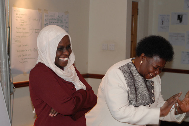 two ladies wearing headscarves are smiling while holding hands together