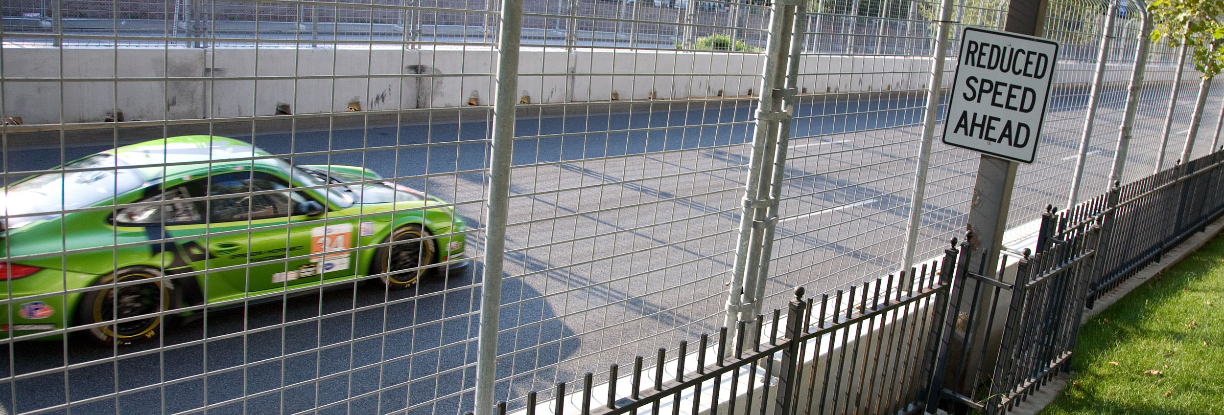 a green car is driving behind a fenced off area