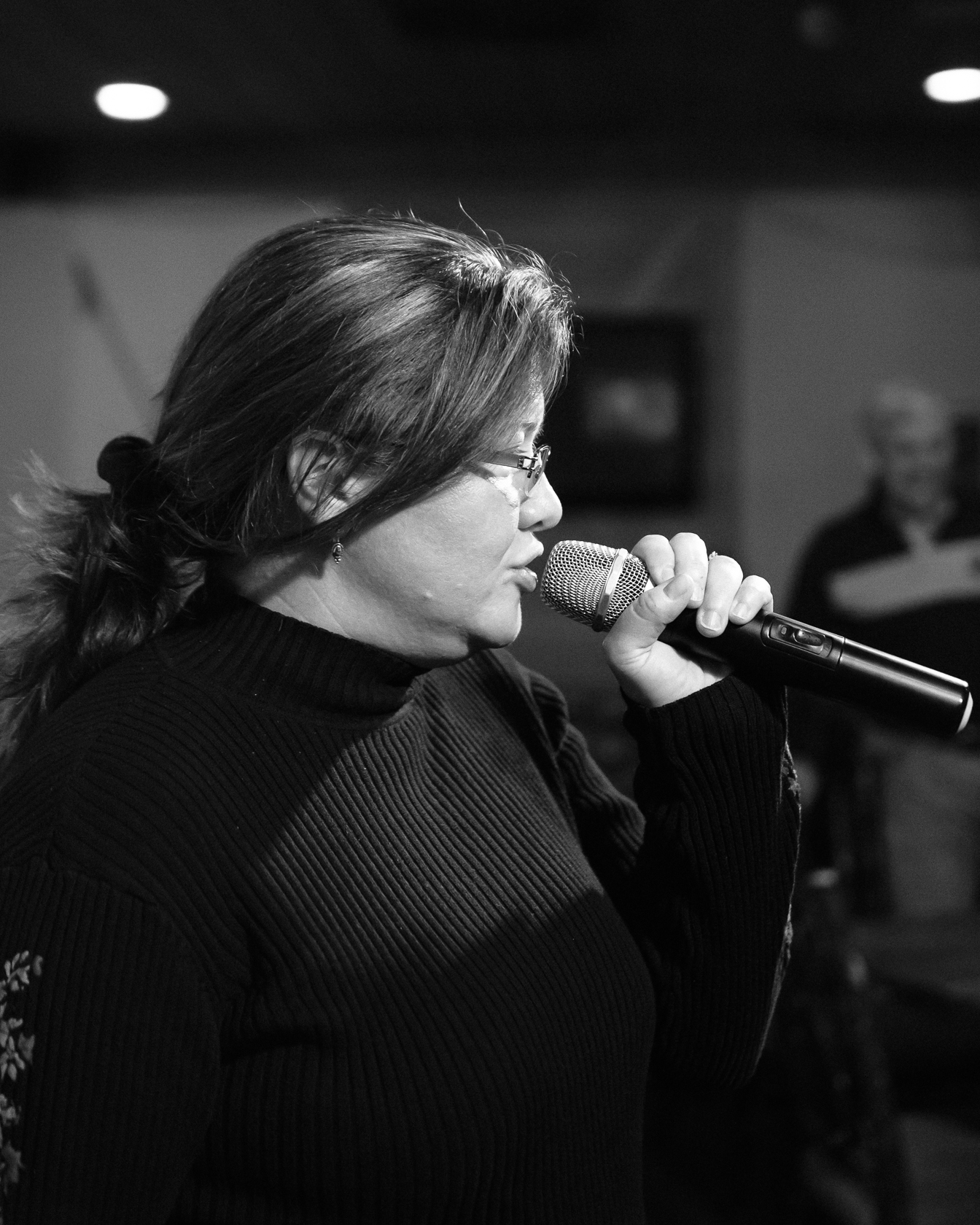 woman in glasses singing into microphone while others watch