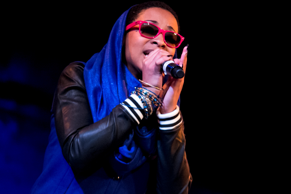 a woman with glasses and a scarf on is holding a microphone