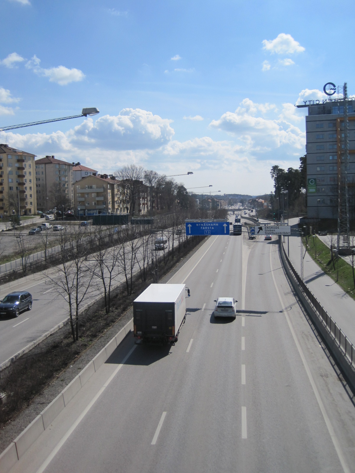 two trucks drive on a street in front of buildings