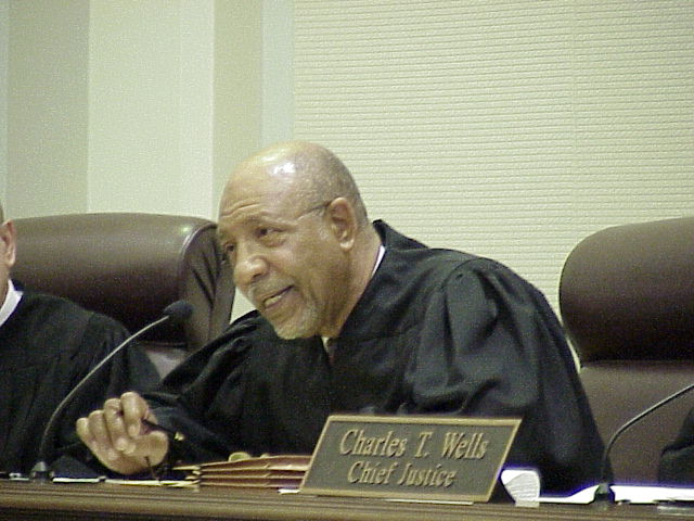 an older man sitting at a table in front of a judge