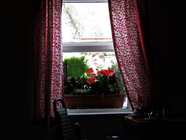 an open window with flowers on a table and a chair in it