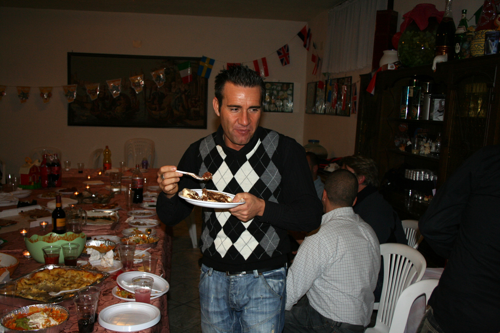 a man in argyle sweater eating food at a dinner table