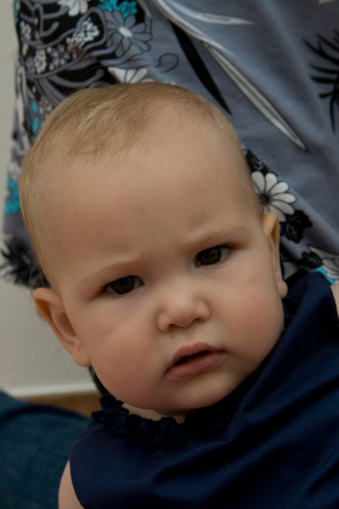 a baby has one eye wide open while wearing a blue dress