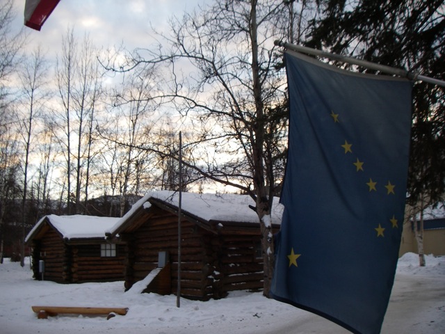 a flag flying from a pole in front of a log cabin