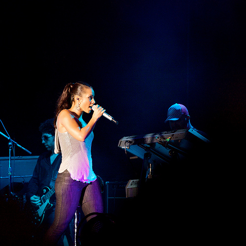 a beautiful young lady holding a microphone while standing in front of a keyboard