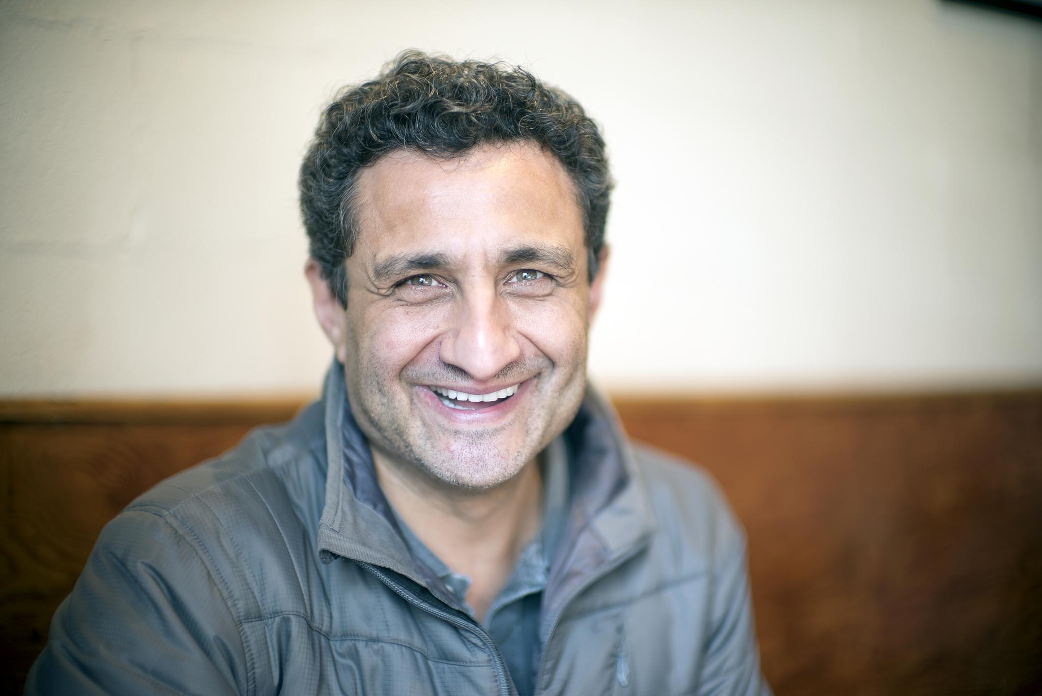 a man with curly hair and a grey shirt smiles at the camera