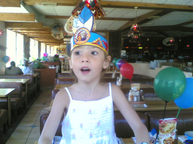 a child with balloons in a restaurant wearing a party hat