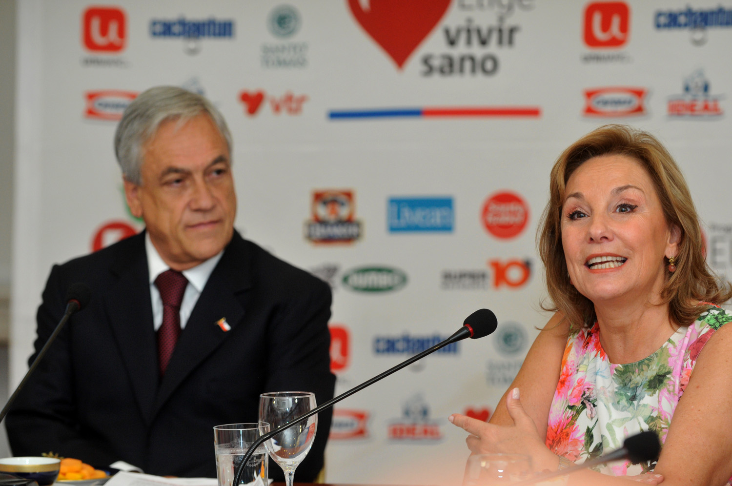 a woman at a press conference talking with a man in the background