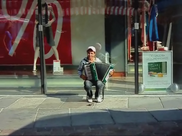 an elderly man sitting in the street holding a piece of music