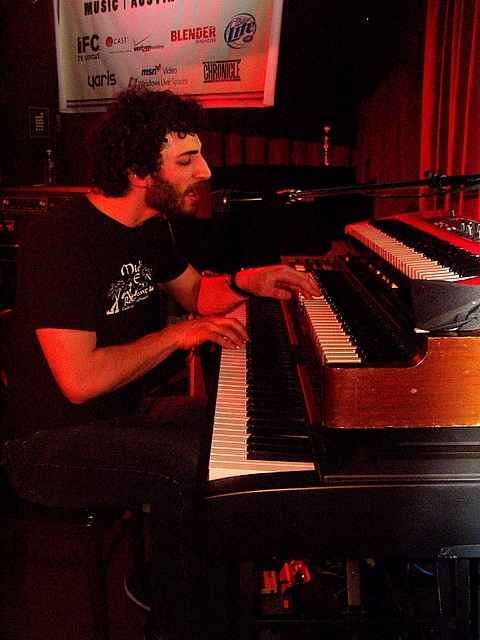 a man is playing a keyboard in front of an event banner