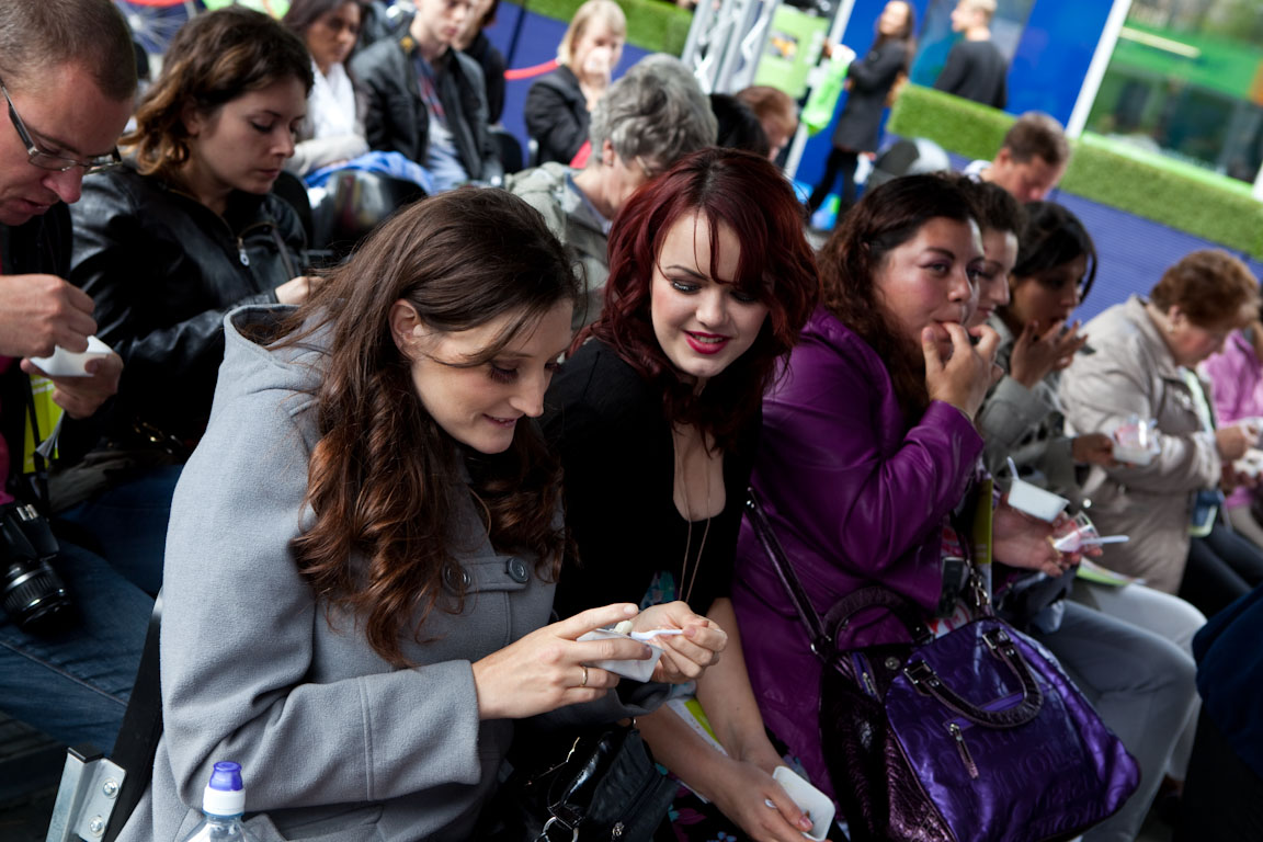 two woman look at their cellphones with the crowd looking on