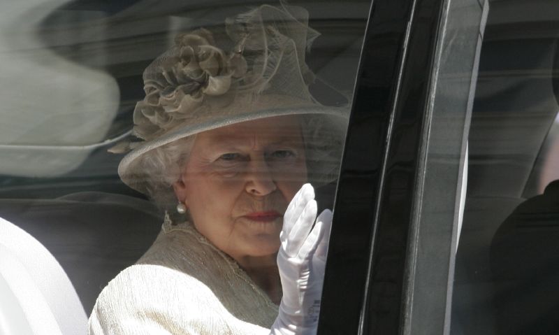 queen elizabeth waves from a car as she wears a white hat