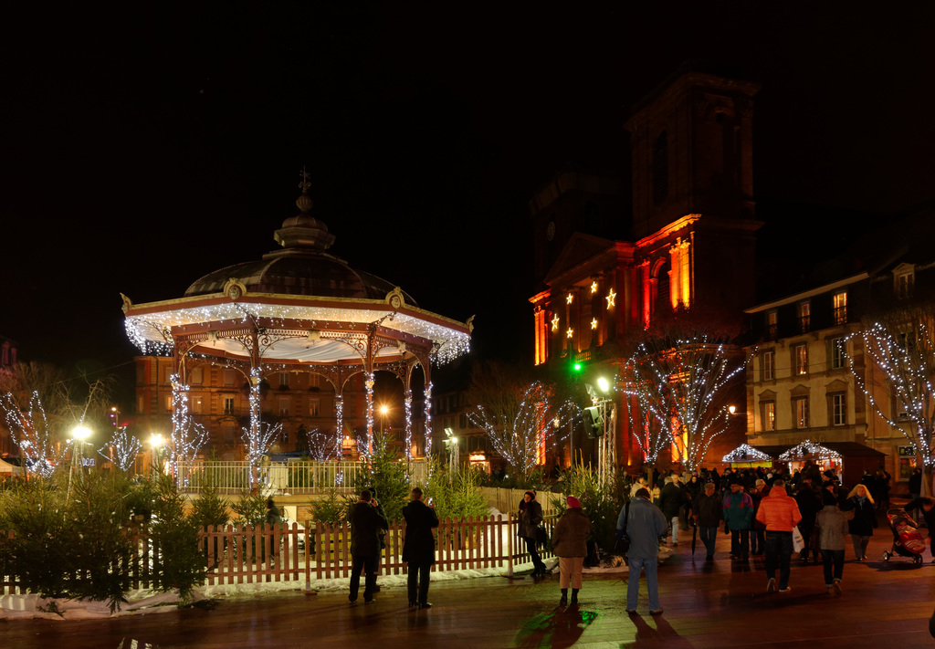 people walk on the walkway between the buildings and buildings decorated with christmas lights